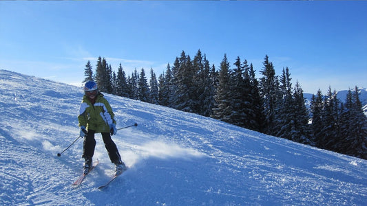 Skier in green jacket skiing down a snowy slope.
