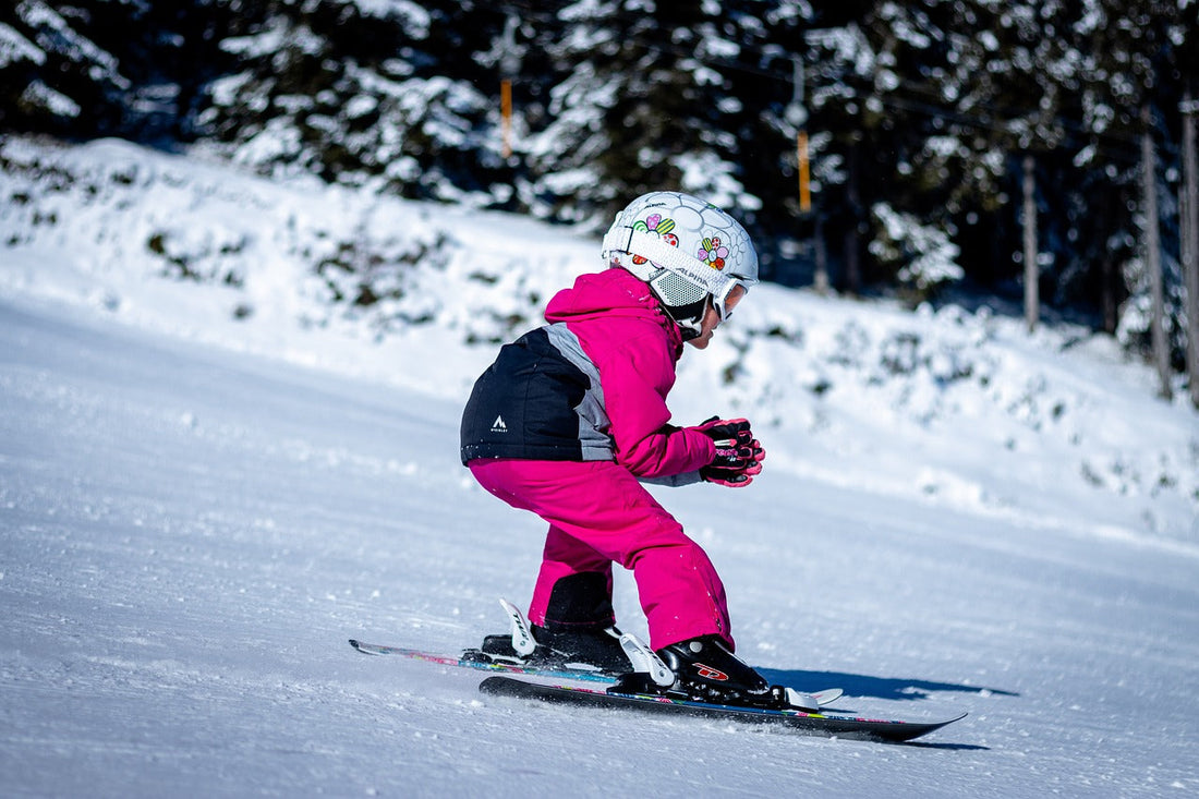 Girls snow suit in pink, skiing on snow-covered slopes with helmet.