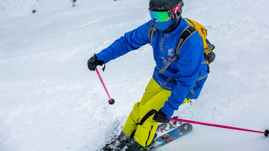Skier in blue jacket and yellow ski pants, skiing in snowy terrain.
