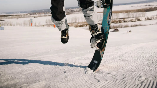 Snowboarder in grey pants jumping on snow slope.