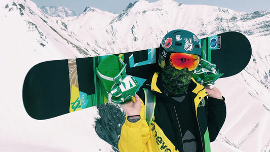 Snowboarder wearing yellow jacket with snowboard in snowy mountain landscape.