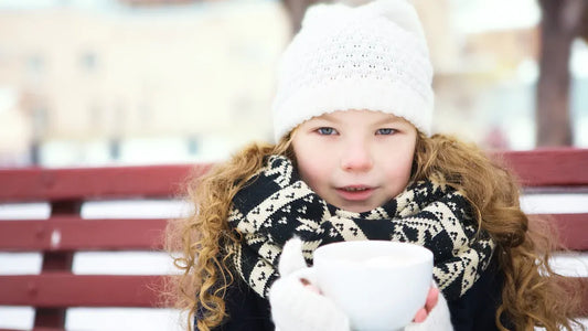 Winter outfit for girls with white hat, gloves, and scarf, holding a warm cup.