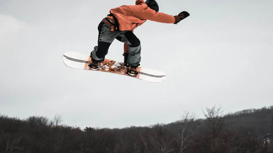 Man wearing baggy snowboard pants while jumping on snowboard.
