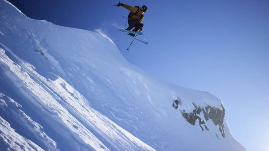 Skier performing a jump off a snowy cliff under clear blue skies.