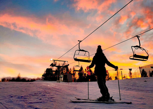 Skier under ski lift at sunset with vibrant sky colors.