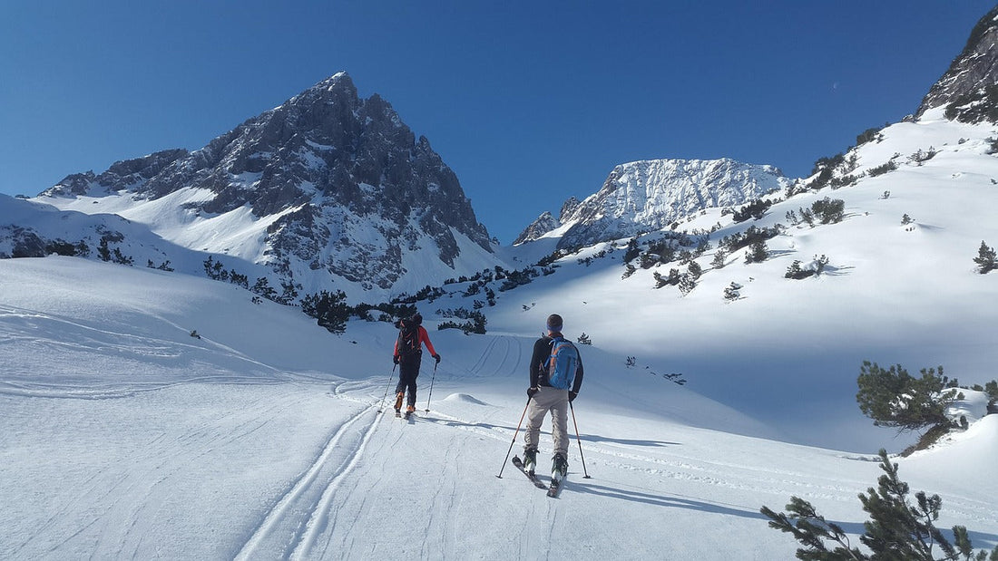 Two skiers on a snowy mountain trail, wearing ski gear and backpacks.